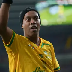 Ronaldinho w żółtej koszulce z zielonymi akcentami, podnosi rękę.