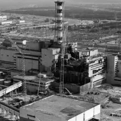 Widok zniszczonego reaktora w Czarnobylu, symbol tragedii i **czarnobyl ofiary**. W tle widać inne budynki elektrowni i żurawie.
