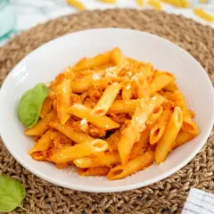 Un plato de macarrones con atún, cubiertos con salsa de tomate y queso rallado, adornado con hojas de albahaca fresca.