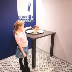 Flicka med flätor pekar på ett huvud som sticker upp ur ett bord på Paradox Museum.