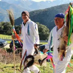 Hombres con trajes blancos y cintas de colores, portando una escoba y una cabeza de cabra, celebran tradiciones de Cantabria.