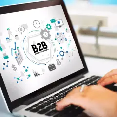 Grafika na ekranie laptopa przedstawia schemat B2B, symbolizujący współpracę biznesową, z ikonami sieci, wykresów i komunikacji.