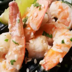 Krewetki na czarnym makaronie, posypane sezamem i ziołami, z kawałkiem limonki.