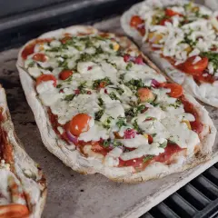 Dwie pizze na kamieniu, z pomidorkami i serem. Dowiedz się, jak przełożyć pizzę na kamień bez łopatki, by uzyskać idealnie chrupiący spód.