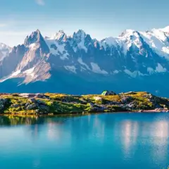 Un lago azul refleja la majestuosa **montaña Mont Blanc** y sus picos nevados. Un campista contempla el paisaje.