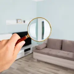 Main d'un homme tenant une loupe pour examiner un appartement. Que vérifier avant d'acheter un appartement ?