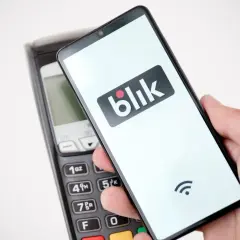 Dłoń trzyma smartfon z logo Blik, zbliżając go do terminala płatniczego. Wygląda na to, że płatność Blik nie działa.