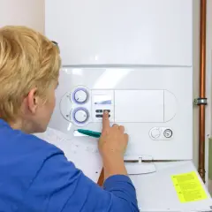 Kobieta sprawdza instrukcję, jak odpalić piecyk gazowy, naciskając przyciski na panelu sterowania.