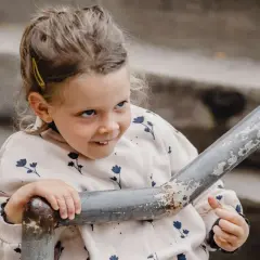 Uśmiechnięta dziewczynka z niepokojącymi zachowaniami 5-latka, oparta o metalową poręcz na schodach.