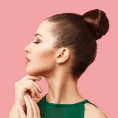 Mujer con moños altos elegantes, perfil sereno, mano en la barbilla, fondo rosa.
