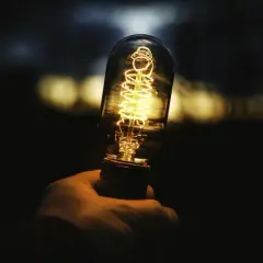 Dłoń trzyma żarzącą się żarówkę Edisona. Zastanawiasz się, ile to wat, gdy świeci 806 lumenów?