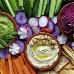 Bunte Auswahl an Dip-Rezepten: cremiger Hummus, grüner Avocado-Dip und Rote-Bete-Dip mit frischem Gemüse und Brot.