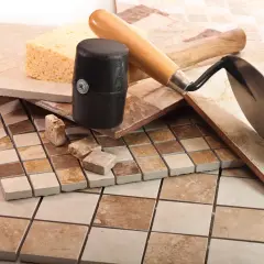 Diverses carreaux de céramique, une éponge, un maillet et une truelle, prêts pour une pose mosaïque sol.