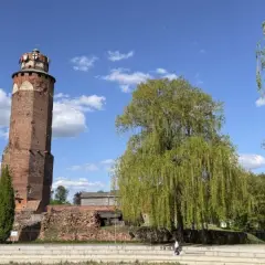 Wieża w Brodnicy Górnej, otoczona zielenią i ruinami, pod błękitnym niebem z chmurami.