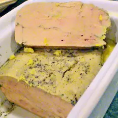 Un délice à partager : un foie gras mi cuit en terrine, parsemé de poivre, prêt à être dégusté.