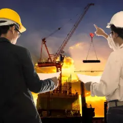 Ingegneri supervisionano un cantiere edile al tramonto, garantendo la sicurezza. Gru solleva materiale.