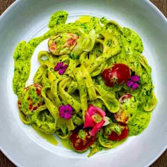 Tagliatelle fresche condite con un cremoso pesto di zucchine, pomodorini e fiori eduli.
