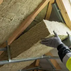 Ręce w rękawiczkach montują wełnę mineralną, docieplenie dachu. Sprawdź, jakie czeka Cię ocieplenie dachu dofinansowanie.