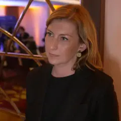Olga Leonowicz, w wieku około 40 lat, w czarnej marynarce, z blond włosami i złotymi kolczykami, stoi przed lustrem.