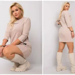Modelka prezentuje beżowe sukienki dzianinowe plus size z rękawem 3/4 i wysokimi kozakami.