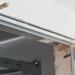 Montaż drzwi ukrytych w ścianie. Metalowa futryna i drewniane kliny podtrzymują konstrukcję.