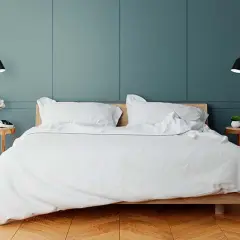 Elegancka sypialnia z białym pościelonym łóżkiem. Po obu stronach łóżka, na ścianie, zamontowane są czarne kinkiety, które idealnie doświetlają przestrzeń. Na jakiej wysokości kinkiet przy łóżku? To zależy od preferencji, ale tutaj są zamontowane na wy...