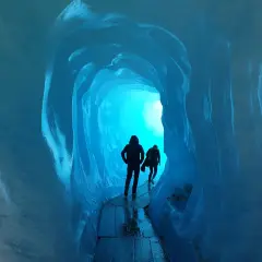 Dwie sylwetki wędrują przez lodowy tunel. Jasne, turkusowe światło przebija się z głębi, tworząc magiczną atmosferę. To jak podróż do wnętrza lodowca, gdzie czas się zatrzymał, a jedynym dźwiękiem jest echo kroków.