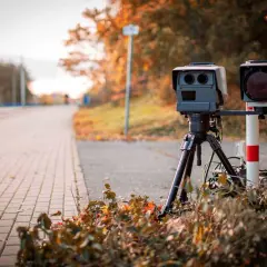 Fotoradar czeka na drodze, by wysłać mandat z fotoradaru. Jesienne liście wokół.