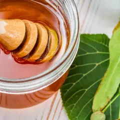 Słoik z płynnym miodem lipowym, drewniana chochla i liście lipy. Miód lipowy kcal - słodka przyjemność.