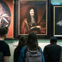 Zwiedzający podziwiają portrety w muzeum sztuki Wrocław. Widać barokowe stroje i peruki.