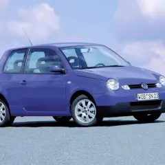 Fioletowy Volkswagen Lupo z tablicą rejestracyjną WOB SN 23 stoi na szarej nawierzchni pod błękitnym niebem z chmurami.