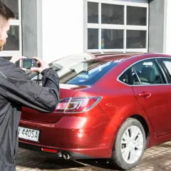Mężczyzna robi zdjęcie czerwonego samochodu, który jest na sprzedaż bezpośrednio od właściciela.
