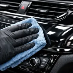 Ręka w czarnej rękawiczce poleruje błyszczące piano black na desce rozdzielczej samochodu, przywracając mu głęboki połysk.