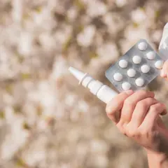 Ręce trzymające spray do nosa, tabletki i chusteczkę, gotowe na walkę z alergią.
