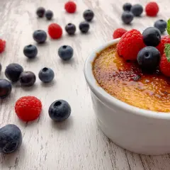 Creme brulee rezept: Ein cremiges Dessert mit karamellisierter Zuckerkruste, garniert mit frischen Beeren und Minze.