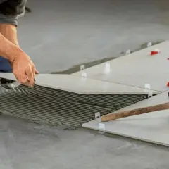 Pose de carrelage mal posé, avec de la colle visible et des cales rouges. Un marteau repose sur une des dalles.