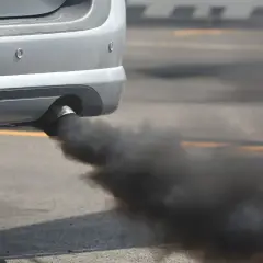 Humo negro al arrancar diésel, una nube densa sale del tubo de escape de un coche plateado.