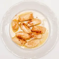 Pyszne pierogi leniwe bez ziemniaków, polane masłem i posypane cynamonem, na białym talerzu.