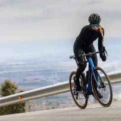 Kobieta w kasku i okularach jedzie na rowerze z niebieskim, aerodynamicznym nadwoziem. Silnik umieszczony centralnie zapewnia moc podczas podjazdu.