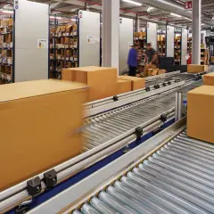 Pudełka na taśmie w magazynie, gotowe do wysyłki. W tle regały z towarem, sugerujące dużą liczbę zamówień i potencjalny **back order**.