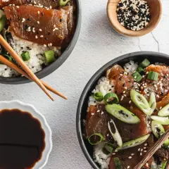 Two bowls of delicious tuna rice don, garnished with sesame seeds and green onions, are ready to be enjoyed with chopsticks.