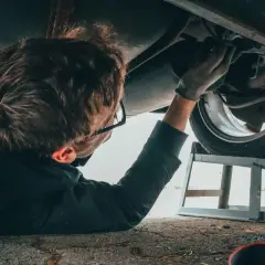 Mechanik podnosi auto sciaga na prawa strone, by naprawić podwozie. W tle puszka WD-40.