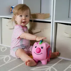 Uśmiechnięta dziewczynka bawi się skarbonką-świnką. To dla niej będzie pierwsze becikowe, gdy nauczy się oszczędzać.