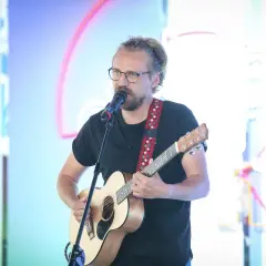 Mężczyzna w okularach gra na gitarze i śpiewa do mikrofonu. Chciałbyś, żeby ktoś powiedział mu "weź się przytul".