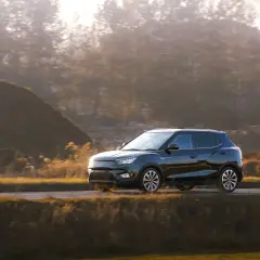 Czarny hatchback jedzie drogą wśród jesiennych wzgórz i drzew.