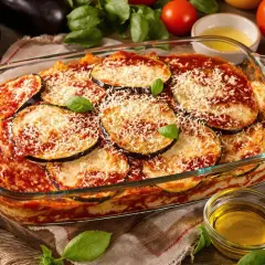 Aubergines à la parmigiana, une véritable recette italienne, dans un plat en verre, garnie de parmesan râpé et de feuilles de basilic frais.