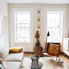 A bright living room with a sofa, fluffy rug, and two windows, demonstrating how to make a small space feel large with light and airy decor.