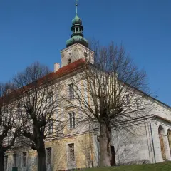 Dawny pałac w Oleśnicy Małej z charakterystyczną wieżą i arkadowym krużgankiem, otoczony nagimi drzewami.