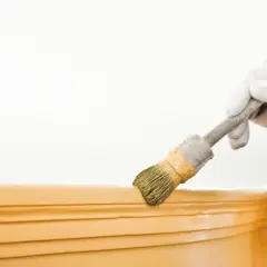 Ręka w białej rękawiczce wykonuje malowanie sztukaterii pędzlem.