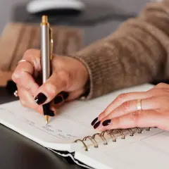 Kobieta pisze w notatniku, planując swoje finanse i rozważając poręczenie kredytu hipotecznego.